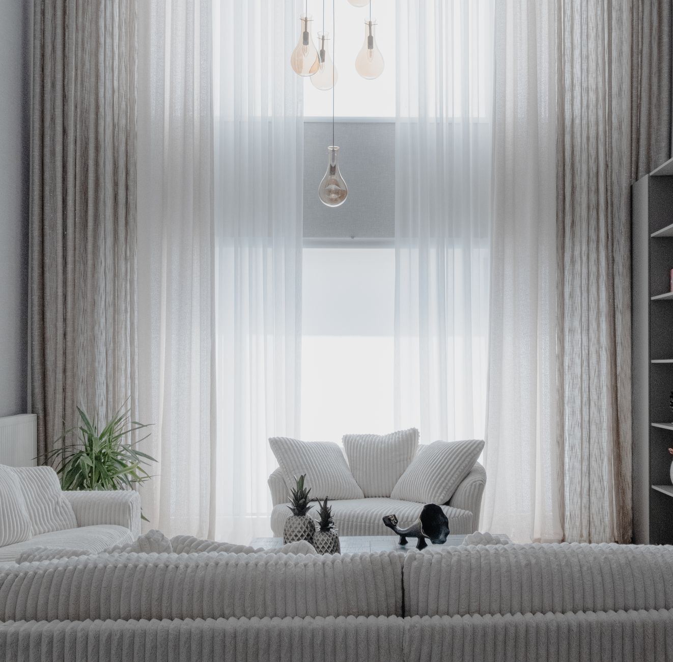 A furnished living room between guests, cushions set square on a linen sofa, a folded blanket over one arm, a low table with a tray and a plant, warm daylight through sheer curtains at the far wall